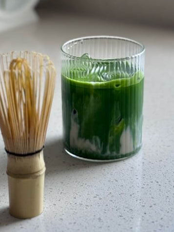Glass of iced matcha latte with traditional bamboo whisk made at home and delivered
